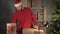 Small business owner Santa Claus holding a gift box on Christmas Eve tying a red bow while sitting at the table late at