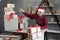 Small business packing goods at home. A man in a Santa Claus hat counts boxes with gifts while sitting at a table on