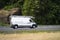 Small cargo van with ladders on the roof driving to point of business on the road with grass and rock background