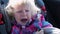 Small Caucasian child girl with curly hair in a warm jacket sits in a child seat, wearing a seatbelt riding in a car