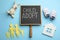 Small chalkboard with phrase CHILD ADOPT, toys, baby shoes and paper family figure on light blue background, flat lay