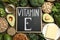 Small chalkboard with phrase Vitamin E and products on wooden table, flat lay