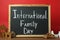 Small chalkboard with text International Family Day, wooden house models, people figure and toy car on brown table against red