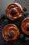 Small cheesecakes covered with chocolate with the addition of fresh blackberries on a cooling tray on a black background,