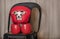 A small chihuahua dog in red boxing gloves and a protective helmet sits on a chair and looks into the camera warily.