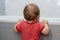 A small child in the bathroom looking into the bath, holding the edge