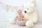 A small child a boy is sitting in a basket in a bear hat with a large Teddy bear