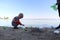 A small child collects trash on the beach. His dad points his finger where to throw garbage. Parents teach children cleanliness.