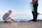 A small child collects trash on the beach. His dad points his finger where to throw garbage. Parents teach children cleanliness.