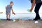 A small child collects trash on the beach. His dad points his finger where to throw garbage. Parents teach children cleanliness.