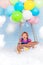 Small child is flying on a bundle of colored balloons filled with helium standing in a wooden pilot basket. located in the sky