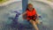A small child in an orange life jacket sitting in a child pool of Aqua Park.