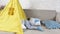 a small child plays at home in a yellow teepee lying on his stomach swinging his legs