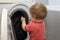 A small child pulls things out of the washing machine, a young assistant