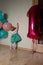 small child reaching for a light switch, near balloons, first birthday. curiosity. girl in a white blue dress