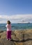 A small child on the shore watching a ship at sea