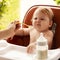 small child sits on a chair and eating with spoon. little smiling girl sits in baby-chair and have a breakfast