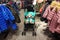 A small child sits in a stroller in a mall store in the midst of rows of clothes