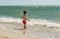 A small child stands on the seashore in the water and looks at the waves. Knows the world,