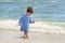 A small child in a striped robe is standing on the seashore in the water and looks at his wet legs to know the world,