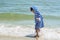 A small child in a striped robe is standing on the seashore in the water and looks at his wet legs to know the world,