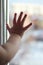 A small child touches a window with his fingers