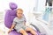 A small child two years old is sitting in a lilac dental chair in a white office