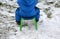 A small child in a winter jumpsuit tries to pull a sledge and still falls, crawling on his knees on the remnants of snow. holding