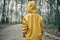 Small child in yellow raincoat with a hood is walking in the dark scary woodland