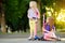 Small children learning to ride scooters in a city park on sunny summer evening. Cute little girls riding rollers.