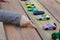 a small children& x27;s hand points to one toy car among a multitude of cars on a wooden red-yellow table