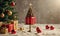 A small Christmas tree is sitting on a cake plate in front of a tree with gifts underneath it.