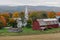 A small church sits on a farm next to a weathered red barn during Autumn