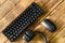 Small compact black computer keyboard next to a computer mouse and headphones on a table made of wooden pine boards. Wireless