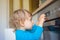 Small and curious child playing with the knobs of the oven in the kitchen. Danger for unattended children, accident prevention at