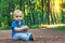 Small cute baby with nipple sits on the footpath in the dreamlike forest all alone. Little boy sitting on the ground.