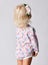 Small cute blonde baby girl in floral jumpsuit with flower decoration in hair standing backwards