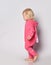 Small cute blonde baby girl in pink warm comfortable jumpsuit walking over grey wall background