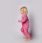 Small cute blonde smiling cheerful baby girl in pink warm comfortable jumpsuit barefoot running over grey wall background