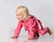 Small cute cheerful blonde baby girl in pink warm comfortable jumpsuit crawling on floor