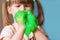 A small, cute girl is holding a green slime on a blue background. A child plays with a slimy toy at home. Chewing gum in children`