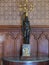 A small dark statue standing near the wall in the room holding a beautiful antique candlestick on its head.