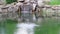 A small decorative waterfall flows with splashes in a pond. Landscaping with stones and water in a park or garden. Natural landsca