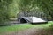 Small delicate wooden arched bridge over a quiet stream deep in the old, thick holiday Park.