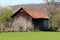 Small dilapidated outdoor storage structure made of wooden boards and concrete building blocks surrounded with grass and dense