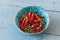 Small dried red chilis in a blue bowl on light blue background