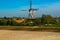 Small Dutch village, wind mill and fruit orchards with spring blossom along dam in Betuwe, Netherlands