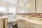 Small elongated bathroom with white porcelain sink embedded in veined marble base, frameless mirror, light tile with valances, and