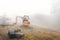 A small excavator Caterpillar 303.5D CR parked on a construction site in a misty autumn landscape.