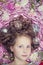 A small fair-haired girl lying on a pink silk fabric with a Christmas garland and Christmas toys around her head